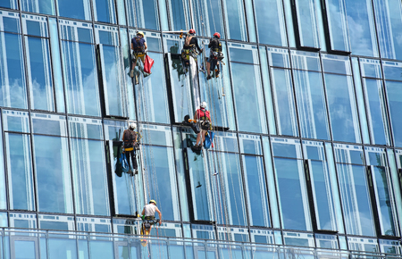 Group of construction workers working at height on modern commercial skyscraper, reflection of the sky and clouds on the glass, teamworkの写真素材