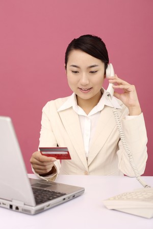 Woman referring to credit card while talking on the phoneの写真素材