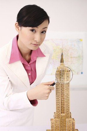 Businesswoman holding magnifying glass near empire state building modelのeditorial素材