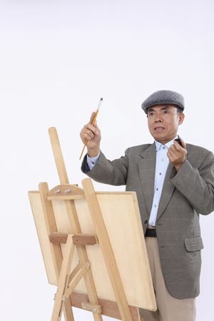Senior man smoking pipe while paintingの写真素材