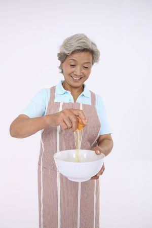 Senior woman cracking egg into bowlの写真素材
