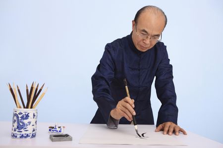 Senior man in traditional clothing writing calligraphyの写真素材