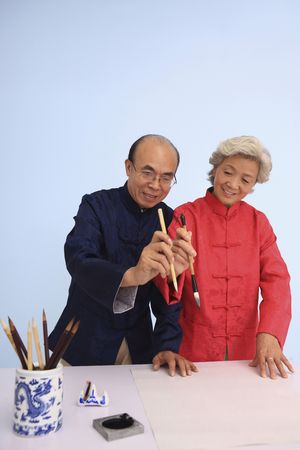 Senior man teaching senior woman how to hold chinese calligraphy brushの写真素材