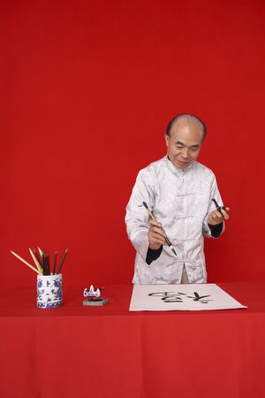 Senior man writing calligraphy while smoking pipeの写真素材