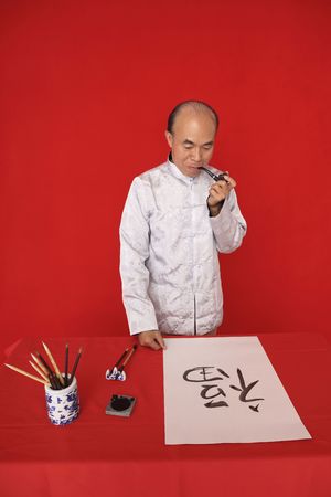 Senior man smoking pipe while looking at his calligraphy artworkの写真素材