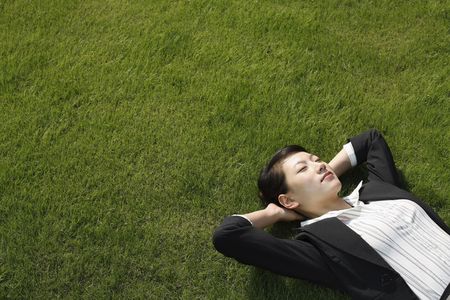 Businesswoman lying down on grassの写真素材