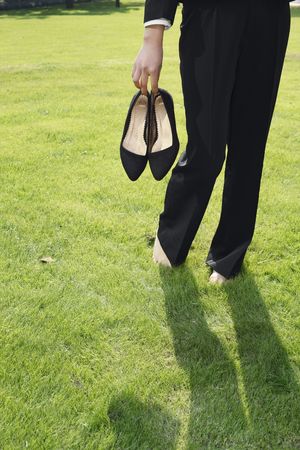 Businesswoman holding heels while walking barefoot on grassの写真素材