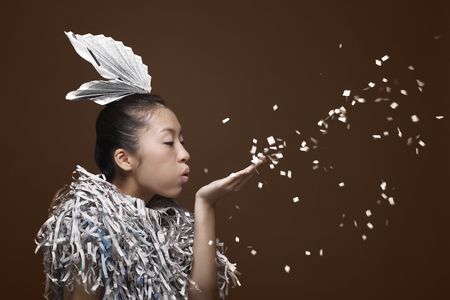 Woman wearing newspaper accessory and shredded newspaper collar blowing paper confettiの写真素材