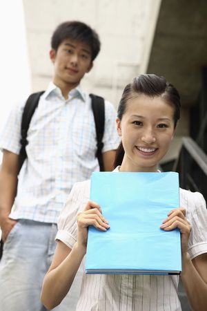 Woman smiling and holding book, man standing in the backgroundの写真素材