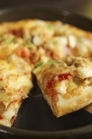 Pizza on pan with slice lifted by spatulaの写真素材