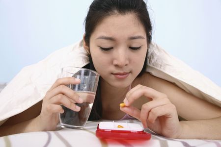 Woman lying forward on bed holding medicationの写真素材