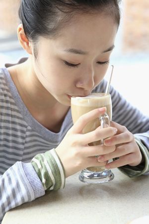 Woman drinking latte in tall glass mugの写真素材