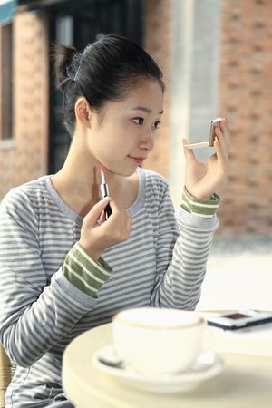 Woman applying lip gloss while looking at compact mirrorの写真素材