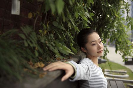 Woman sitting on wooden bench, looking awayの写真素材