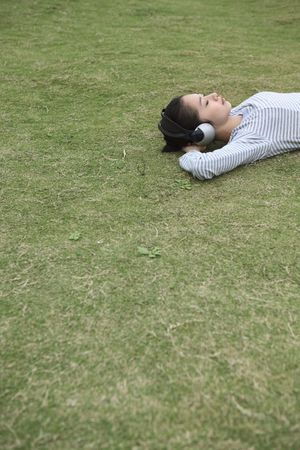 Woman lying on grass listening to headphonesの写真素材