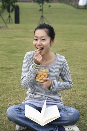 Woman enjoying cookies with book on her lapの写真素材