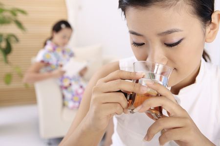 Young woman drinking tea, another woman reading book in the backgroundの写真素材