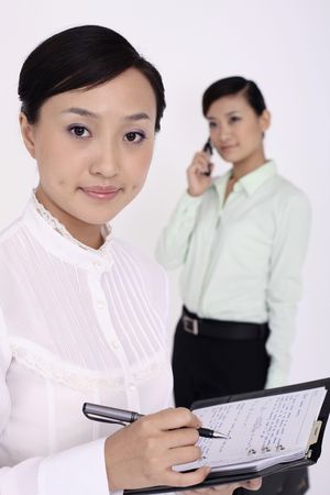 Young woman writing on organizer, another woman talking on the phone in the backgroundの写真素材