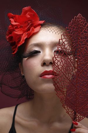 Woman with net and flower decorating her hair holding red leaf over faceの写真素材
