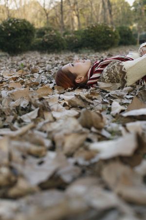 Woman holding book lying on ground covered with dried leavesの写真素材