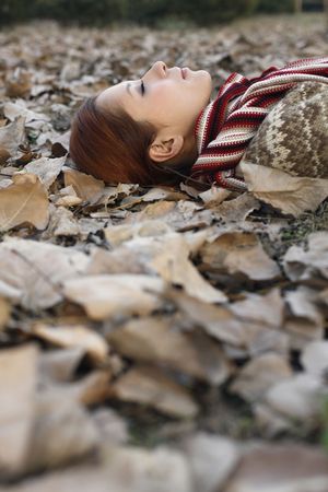 Woman lying on ground covered with dried leaves, closing eyesの写真素材