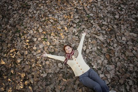 Woman lying on ground covered with dried leaves with arms outstretchedの写真素材