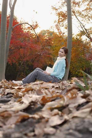 Woman leaning against tree holding bookの写真素材
