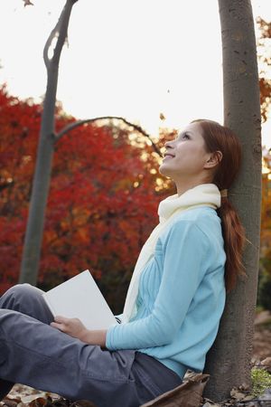 Woman leaning against tree daydreamingの写真素材