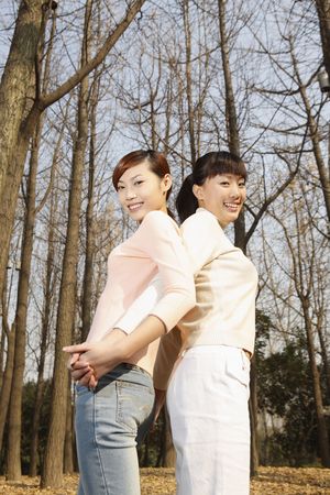 Women holding hands while standing with their backs against each otherの写真素材