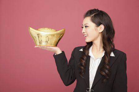 Woman smiling while looking at the gold ingot she is holdingの写真素材