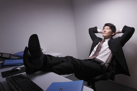 Man with his arms crossed behind his head and legs on the tableの写真素材