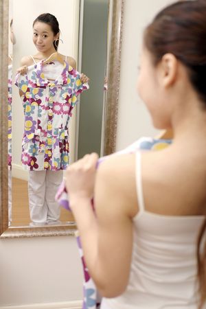 Young woman holding dress while standing in front of mirror