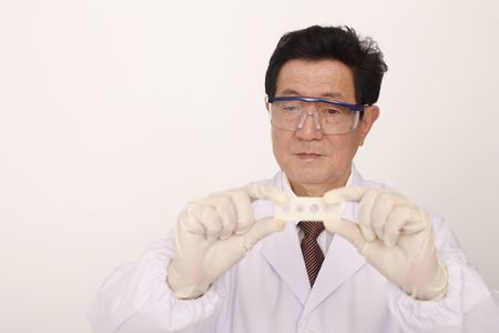 Doctor wearing safety goggles holding slide and magnifying glassの写真素材