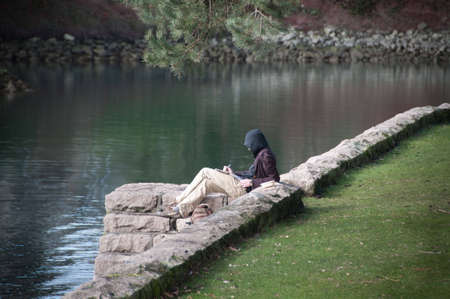 Person writing a note on some paper by the water.の写真素材