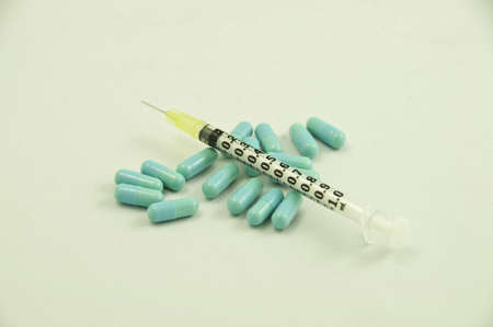 The focus is on the middle of the syringe. Blue pills on a white background.