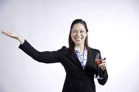 Young business woman holding a glass of wine in her hand, She is of filipino ethnicity. She has her arm strecthed out.の写真素材