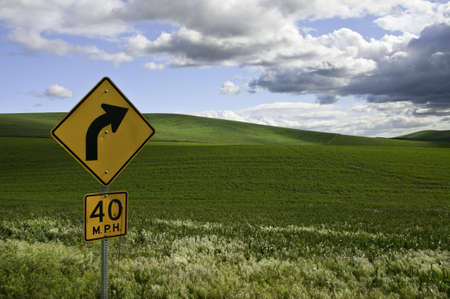 Road sign showing a right turn. Big fluffy clouds are going by.