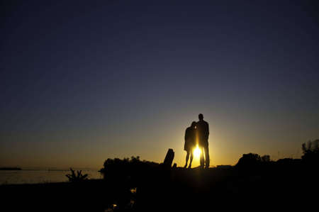 Couple standing by the shore with the sun setting in background of couple standing by the shore with the sun setting in background. S sunburst between the two of them.の写真素材