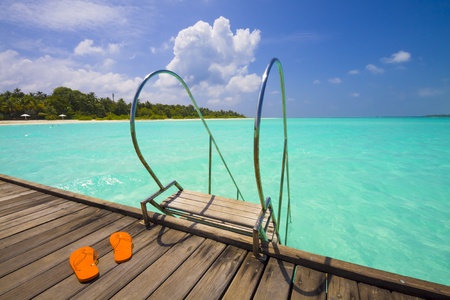 ladder to the sea from a jetty; view to tropical island with beach and palmsの写真素材