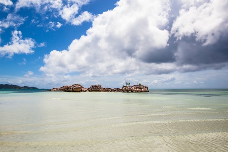little rocky island in the sea under a blue sky with some white clouds, Seychelles
