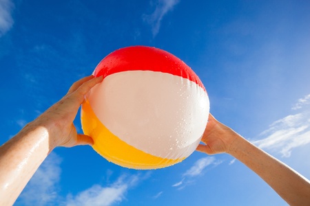 woman holding a red, yellow, white beach ball over her head in the blue skyの写真素材