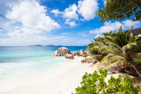 view to a tropical beach with palms, tropical plants, granite rocks, white sand, a turquoise sea and a blue sky with some clouds, La Digue, Seychellesの写真素材