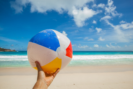 female hand holding a ball at a beautiful beach with a turquoise sea and blue sky, Seychellesの写真素材