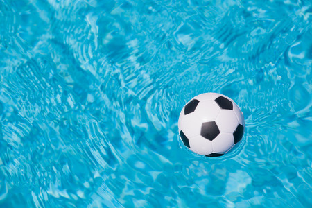 sport background of a little plastic football floating in the blue water of a swimming poolの写真素材
