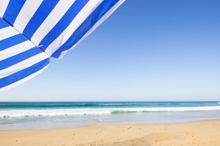 travel background with a blue and white sunshade at an endless white beach with a blue sky and a turquoise sea,  Playa de las Pilas, Fuerteventura, canary islands, Spain, Europeの写真素材