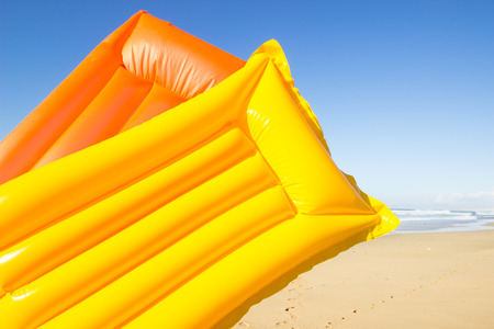 travel background with a yellow and orange air mattress at an endless white beach with a blue sky and a turquoise sea,  Playa de las Pilas, Fuerteventura, canary islands, Spain, Europeの写真素材