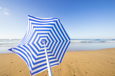 travel background with a blue and white sunshade at an endless white beach with a blue sky and a turquoise sea,  Playa de las Pilas, Fuerteventura, canary islands, Spain, Europeの写真素材