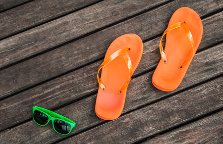 pair of orange flip-flops and green sunglasses on the wooden planks of a jettyの写真素材