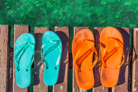 two pair of turquoise green and orange  flip-flops on the wooden planks of a jetty  over the seaの写真素材