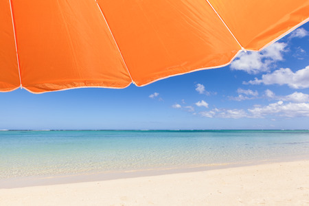 travel background with an orange sunshade, turquoise sea, blue sky and the white sand of a beautiful beach, Mauritius, Africaの写真素材